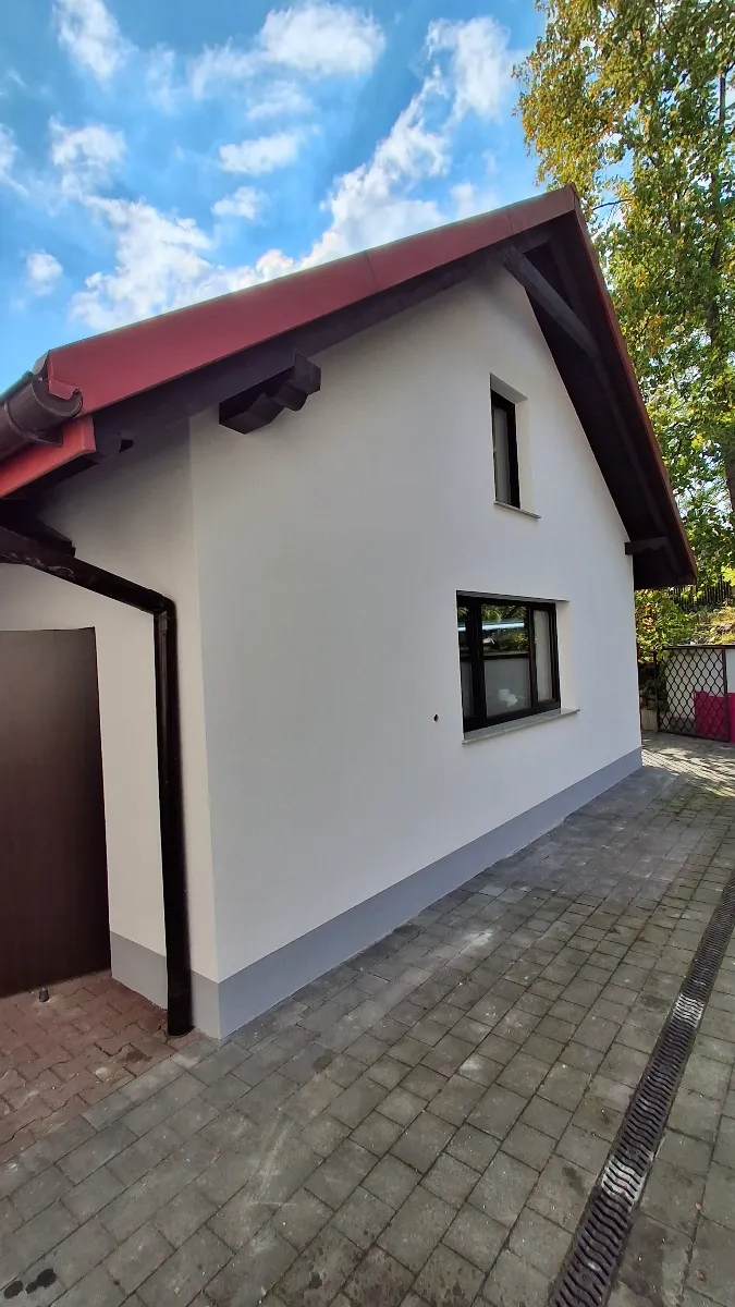 Elewacja domu z nowo pomalowaną białą ścianą, szarym cokołem i czerwoną dachówką