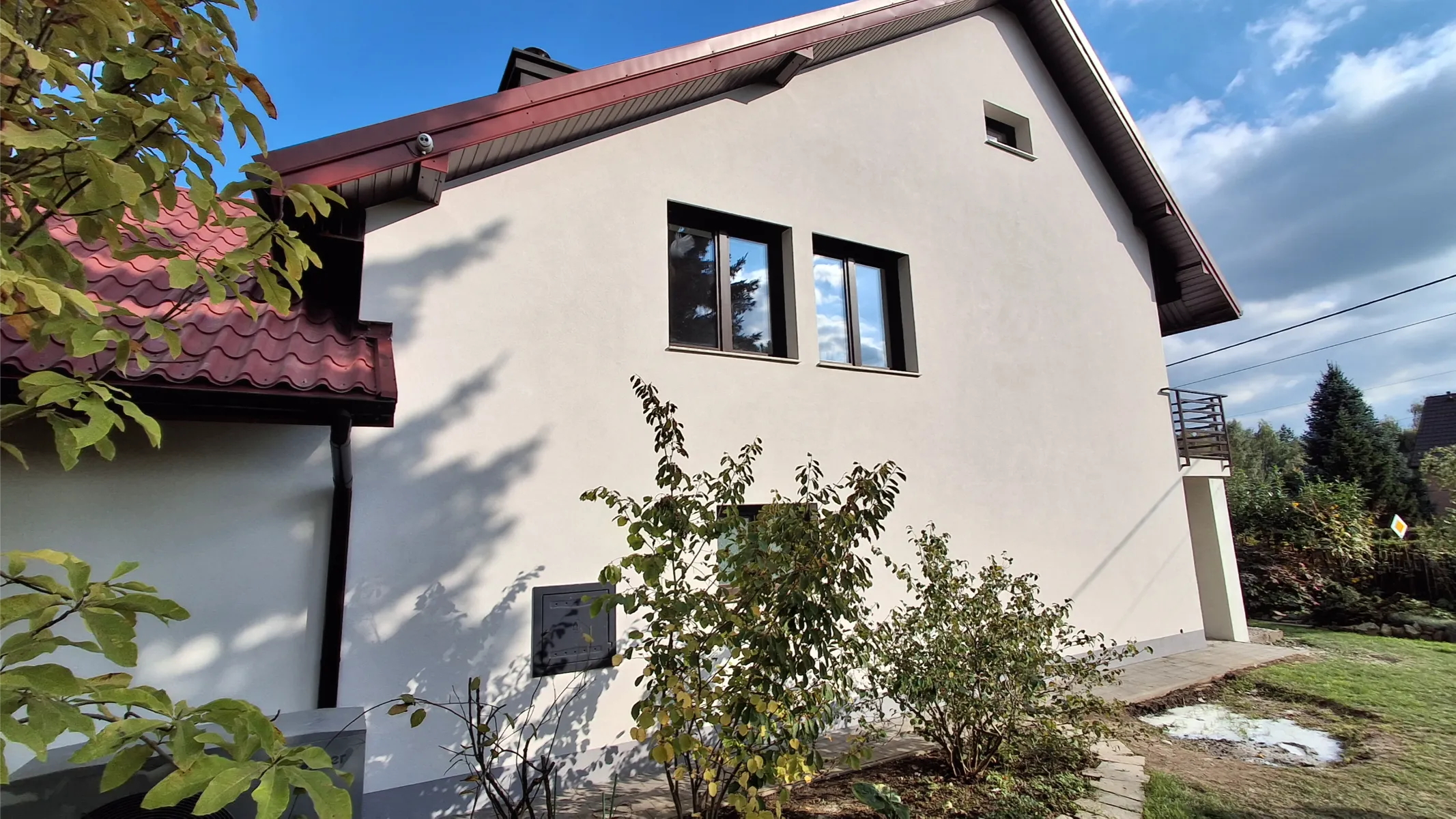 Elewacje domu: biała świeżo wykończona ściana budynku z dwoma oknami i roślinnością