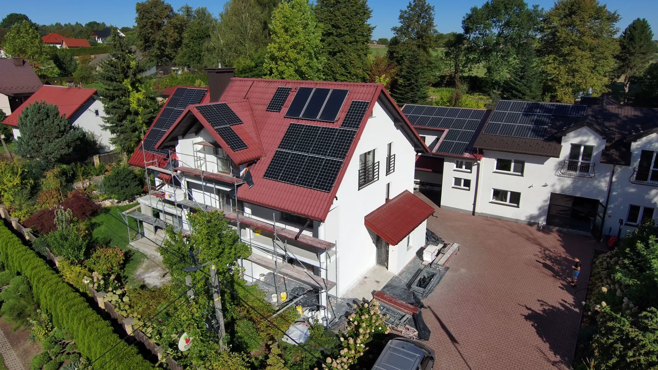 Tynkowanie elewacji domu na rusztowaniu pod czerwonym dachem