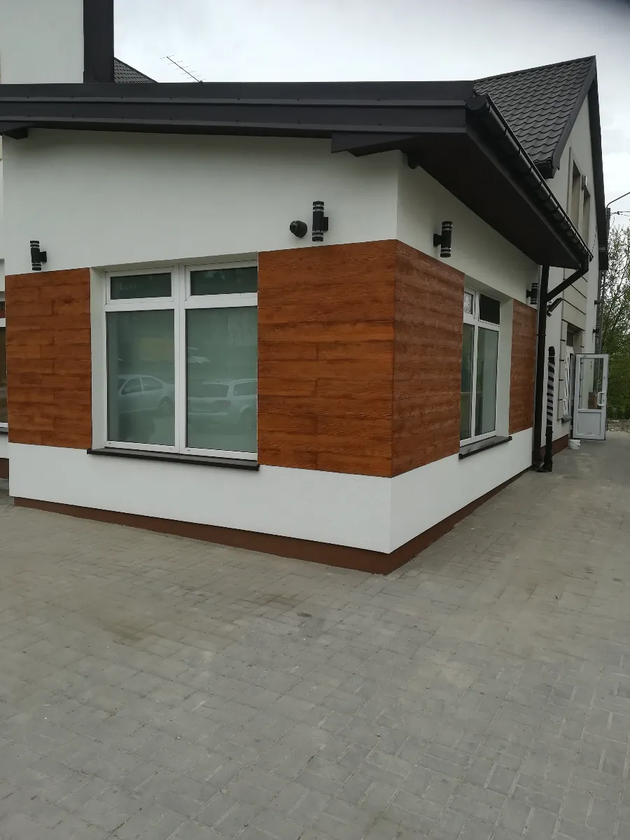 Narożnik budynku z białą elewacją i drewnopodobnymi panelami wokół okien – usługa Elewacje domu