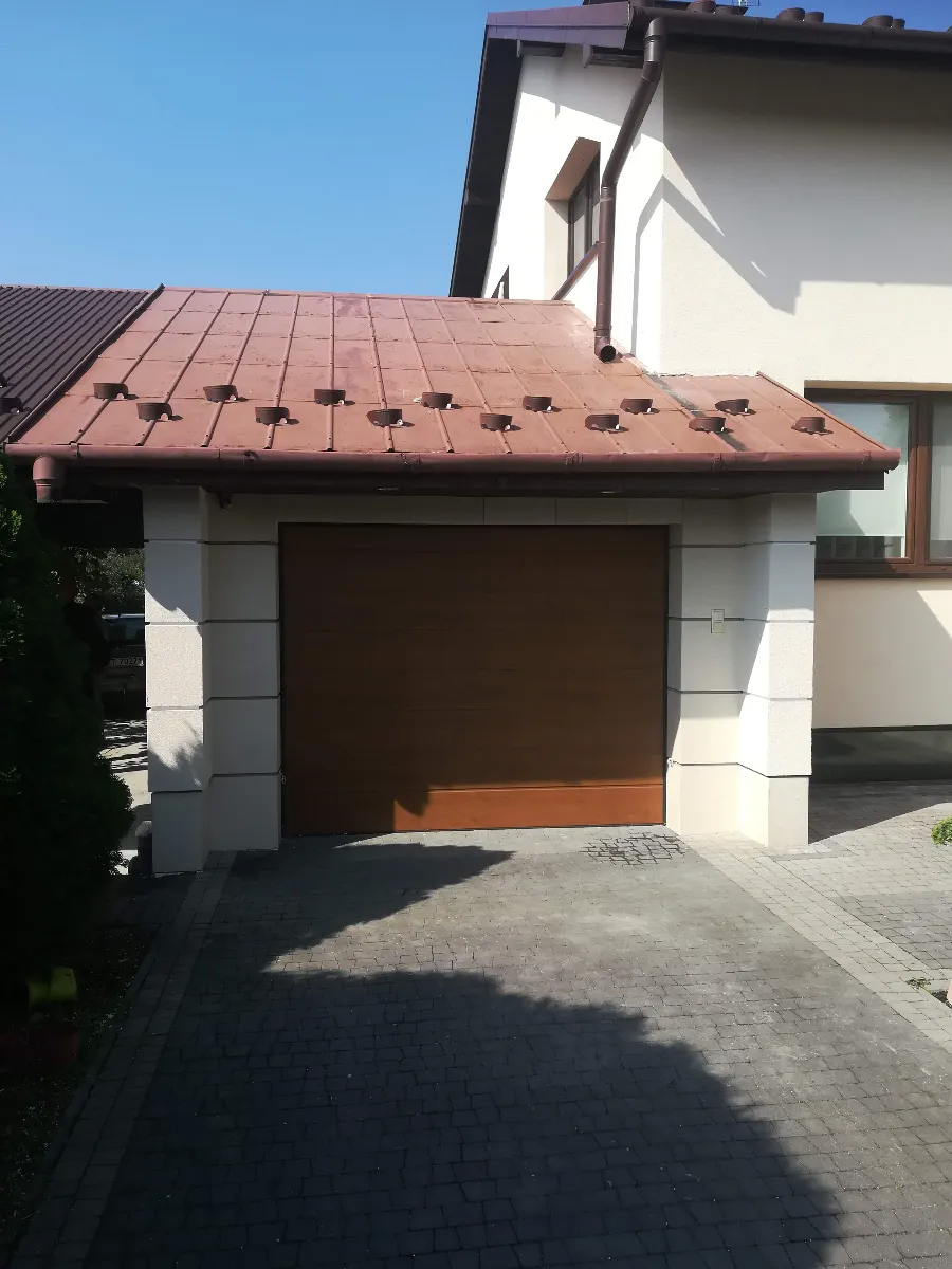 Zamontowana drewniana brama garażowa na podjeździe przed elewacją – montaż drzwi