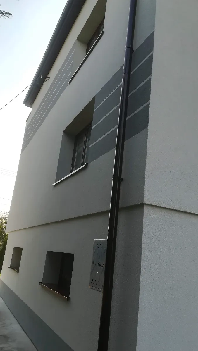 Malowanie elewacji: pomalowana elewacja domu z dekoracyjnymi szarymi pasami i rurą spustową