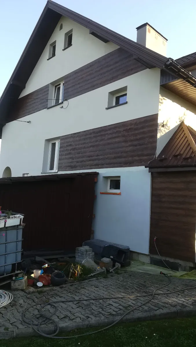 Elewacje domu z drewnianą okładziną i tynkowanymi pasami, narzędzia budowlane na podjeździe