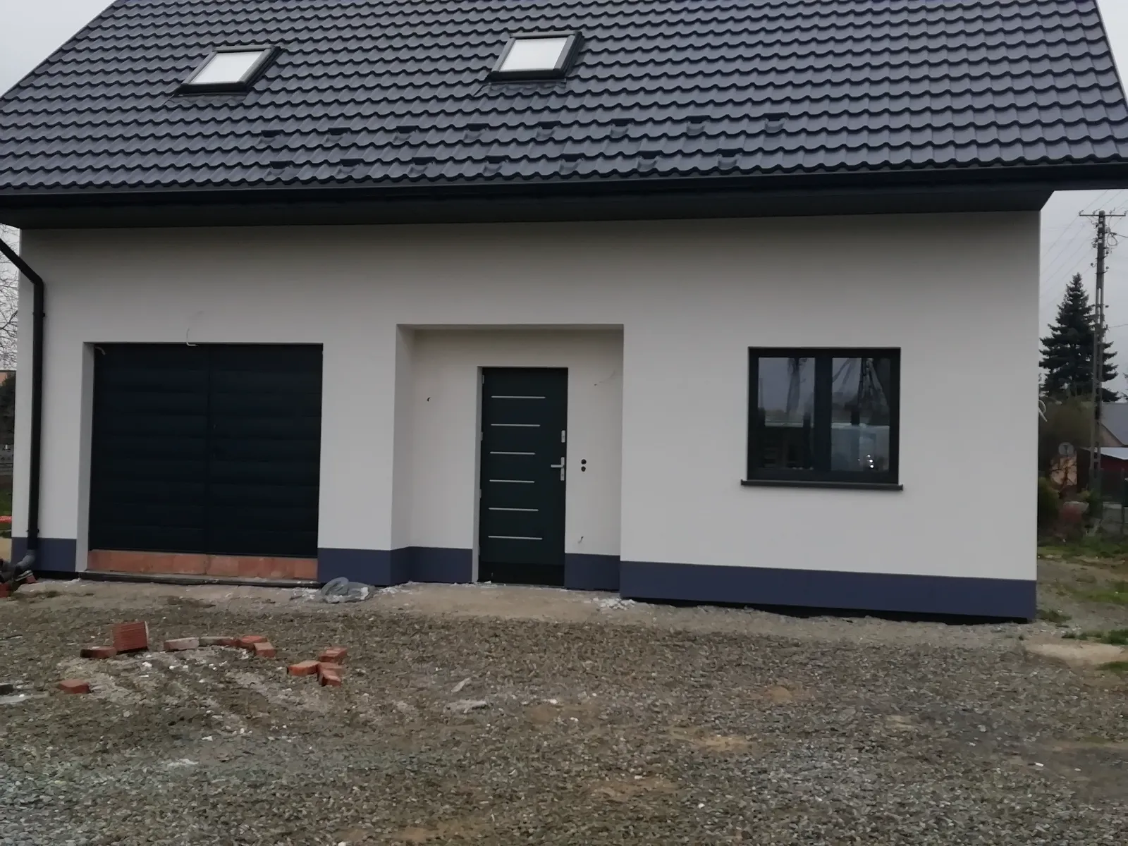 Elewacje domu – biała fasada z czarnym dachem, nowoczesne drzwi oraz okno na parterze