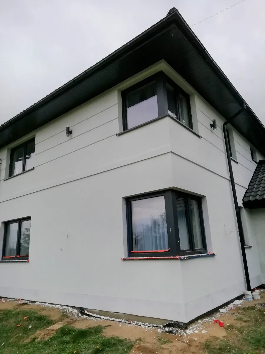 Róg dwukondygnacyjnego domu z nową białą elewacją, czarne ramy okien i dach Elewacje domu