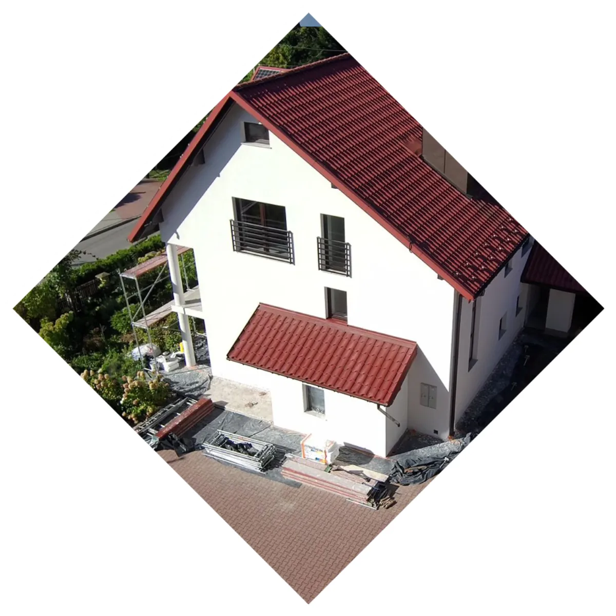 Widok elewacji domu z białym tynkiem, czerwonym dachem, rusztowaniem i materiałami wykończeniowymi