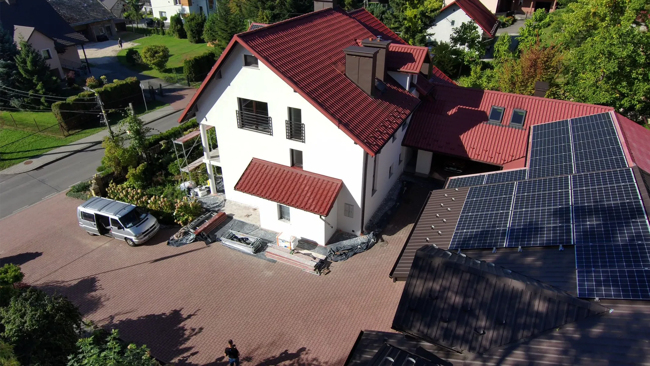 Elewacje domu z rusztowaniem przy białej ścianie i czerwonym dachu, widoczny van i materiały budowlane