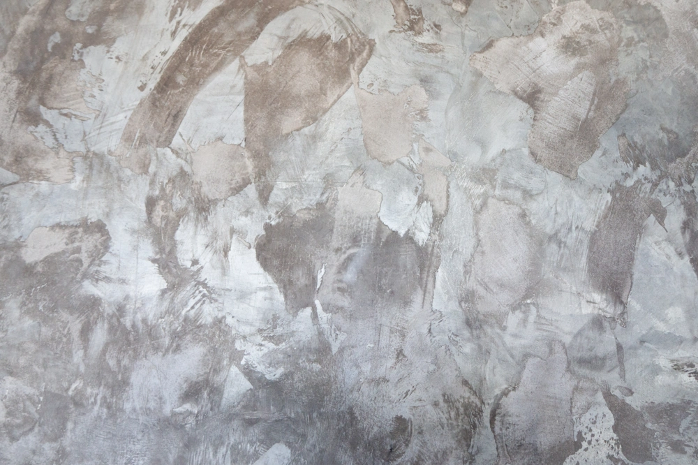 Ściana wykończona stiukiem weneckim o metalicznym szaro-beżowym odcieniu i wyraźnych tynkarskich wzorach