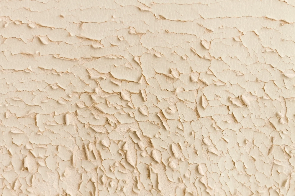 Ściana z łuszczącą się farbą i spękanym tynkiem wymagająca tynkowania