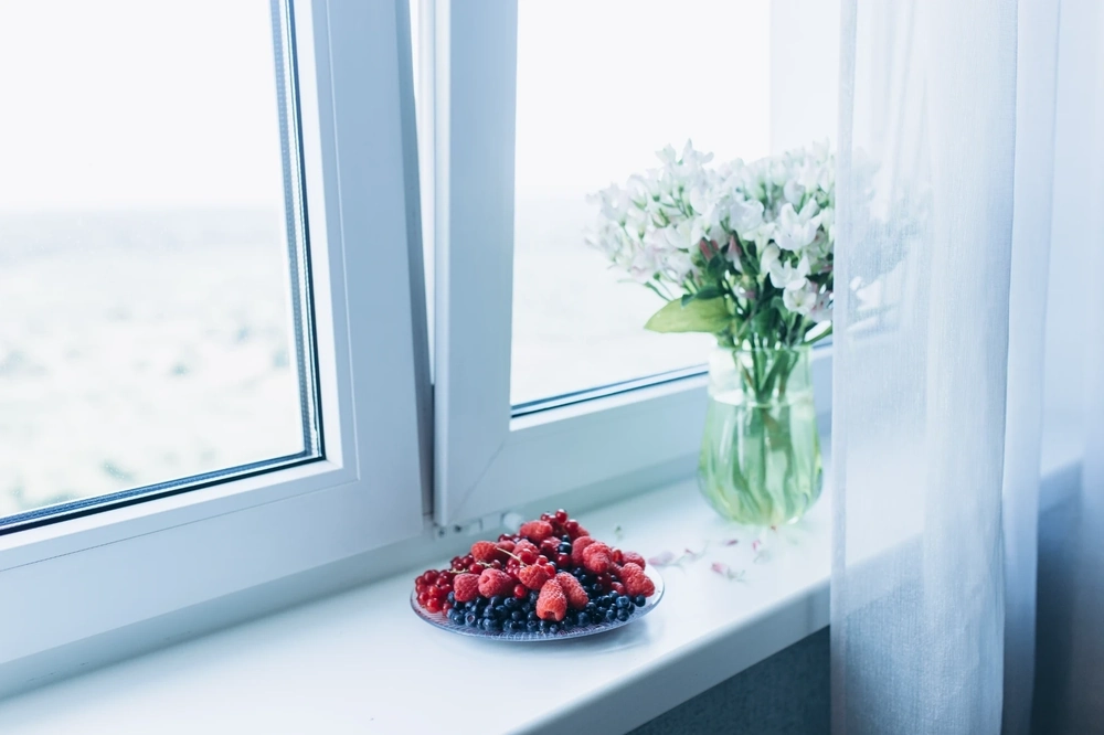 Parapety: biały parapet z talerzem świeżych owoców i wazonem kwiatów przy otwartym oknie