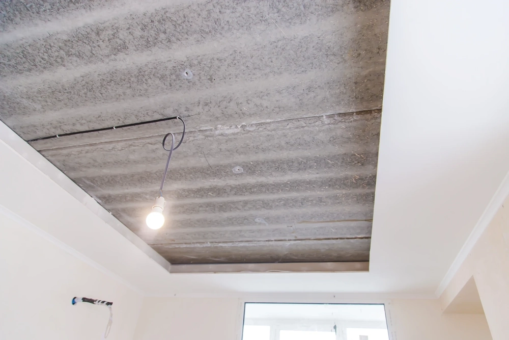 Prace przy sufitach podwieszanych – odsłonięta płyta stropowa z zamocowaną ramą pod konstrukcję i wiszącą lampą roboczą