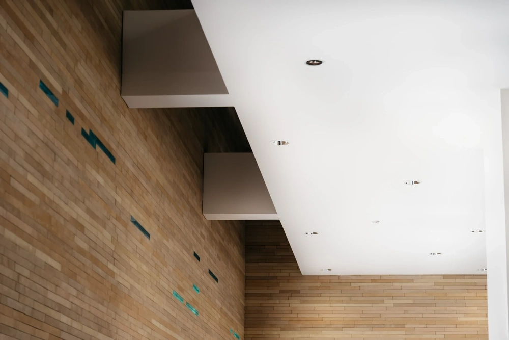 Widok wnętrza z białym sufitem podwieszanym z wpuszczanymi oprawami na tle ceglanej ściany, sufity podwieszane