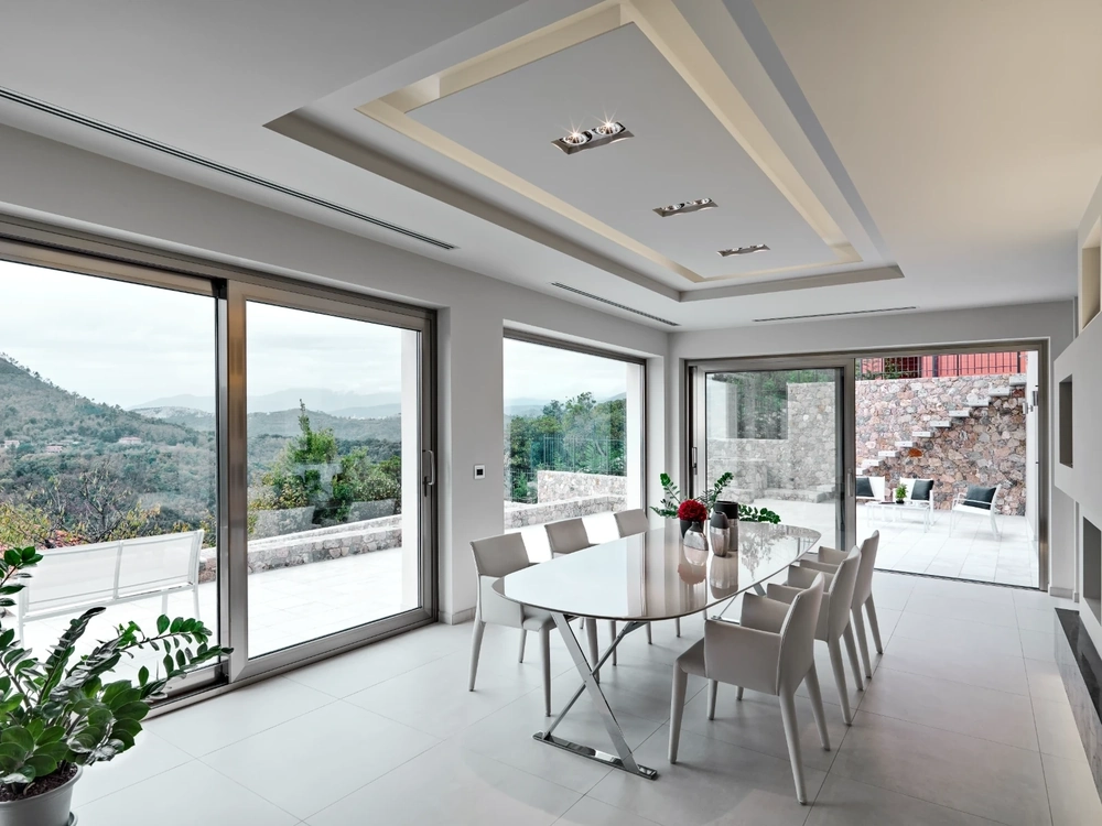 Jasna aranżacja wnętrz jadalni z białym stołem, krzesłami i panoramicznymi przesuwnymi oknami